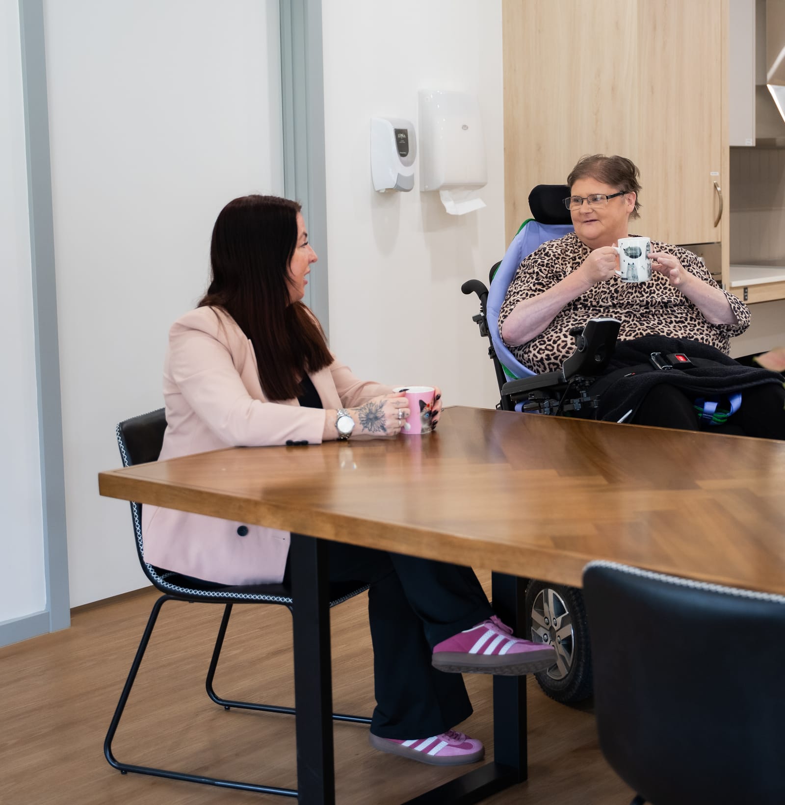 A QB Care participant and staff member sharing a coffee at the office table