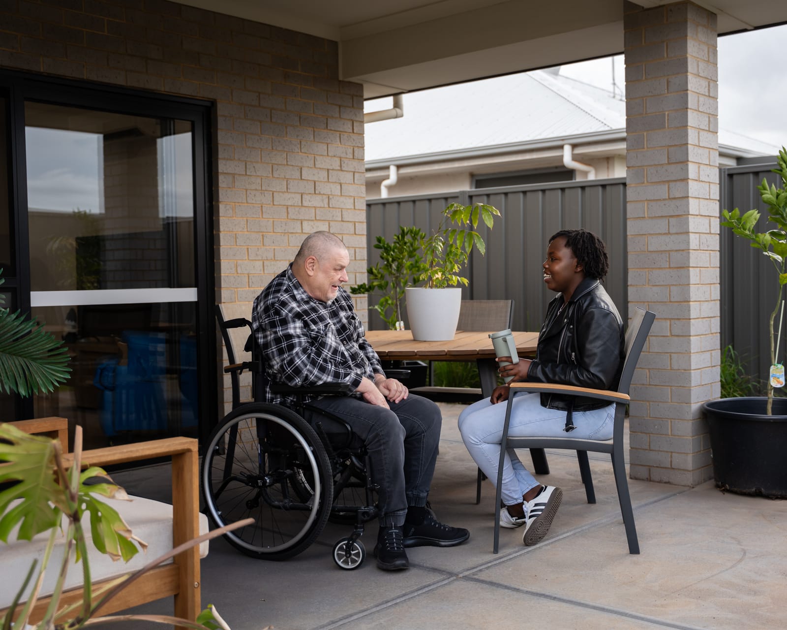 A QB Care participant and support worker talking over a drink on the back patio of his home